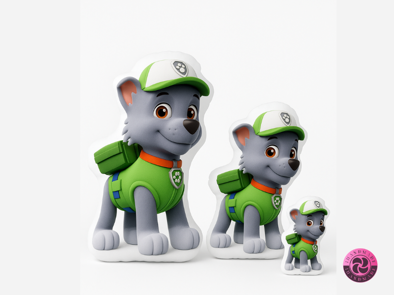 Egyedi formapárna gyerekeknek 1 Három különböző méretű, egyedi mintás Rocky formapárna a Mancs Őrjáratból, zöld ruhában és sapkában, fehér háttéren.