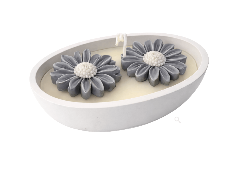 Ovális, fehér tálban öntött krém színű gyertya két szürke, virág formájú díszítéssel és középen elhelyezett kanóccal, letisztult háttér előtt.