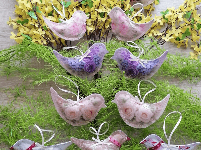 🐣 Névre szóló húsvéti dekoráció – Egyedi, kézzel készült filc tojás, nyuszi és pipi 7 Pasztell madár alakú tavaszi függődíszek lila és rózsaszín virágmintával, zöld mohával és sárga virágzó ágakkal fa háttéren