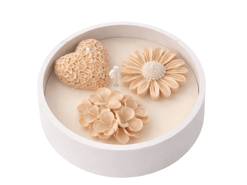 Kerek, fehér tálba öntött krém színű gyertya, tetején barack árnyalatú virág- és szív formájú díszítésekkel, középen kanóccal, letisztult háttér előtt